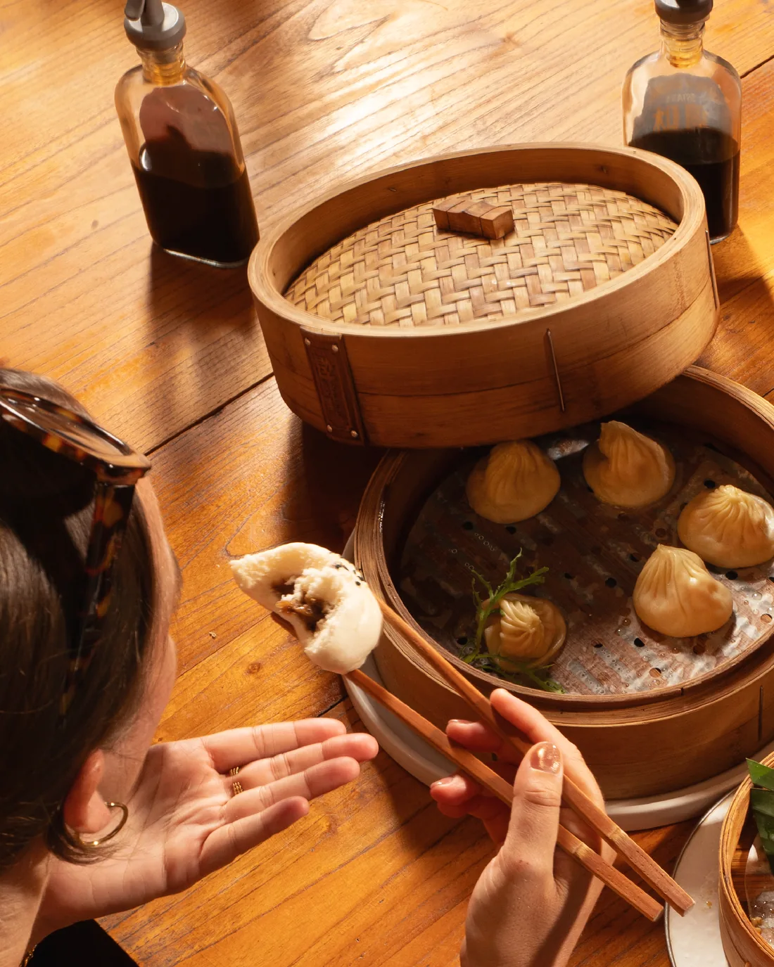 A guest lifting a dumpling with chopsticks over open steamer baskets