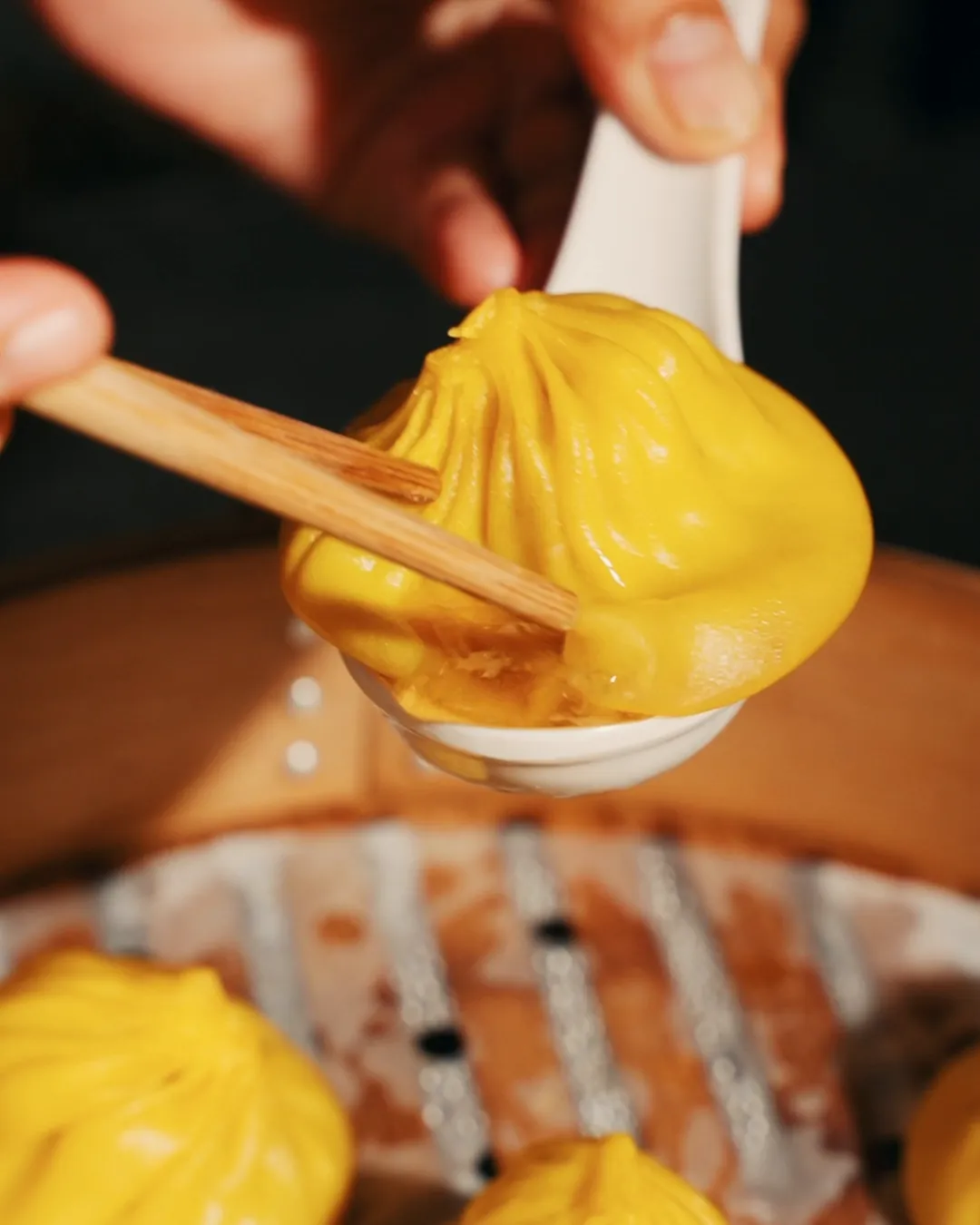A xiao long bao lifted from a bamboo steamer with chopsticks