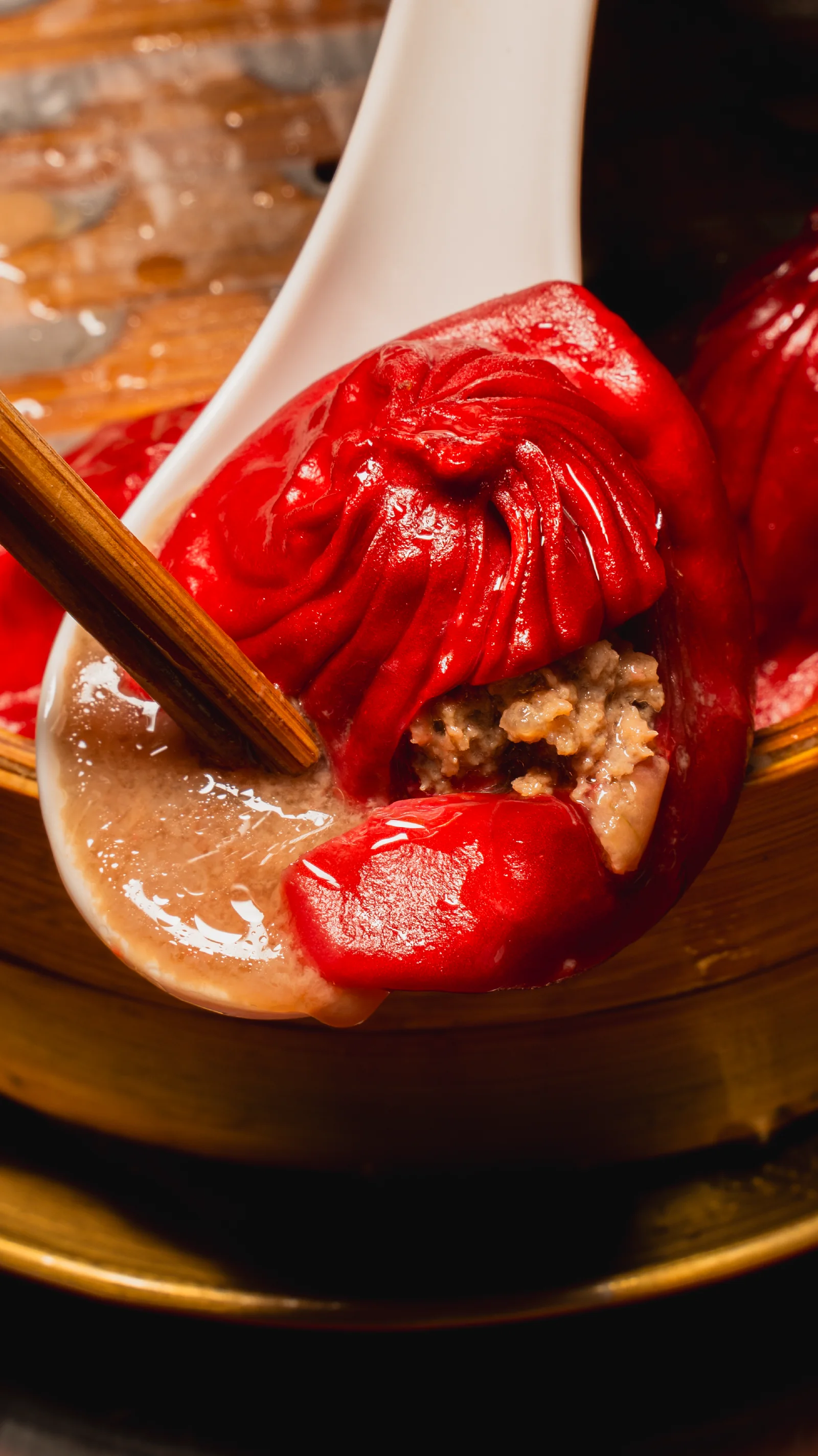A signature red xiao long bao on a spoon lifted by chopsticks